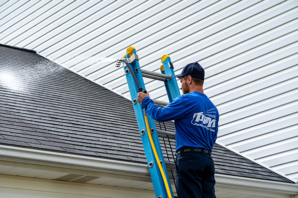 Perfect Power Wash technician performing one of our many professional power washing services. He is treating a roof from a ladder.